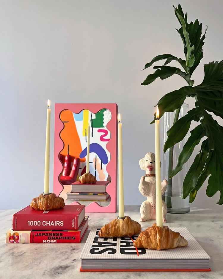mesa com livros apoiados, espelho rosa pequeno e porta vela em formato de croissant