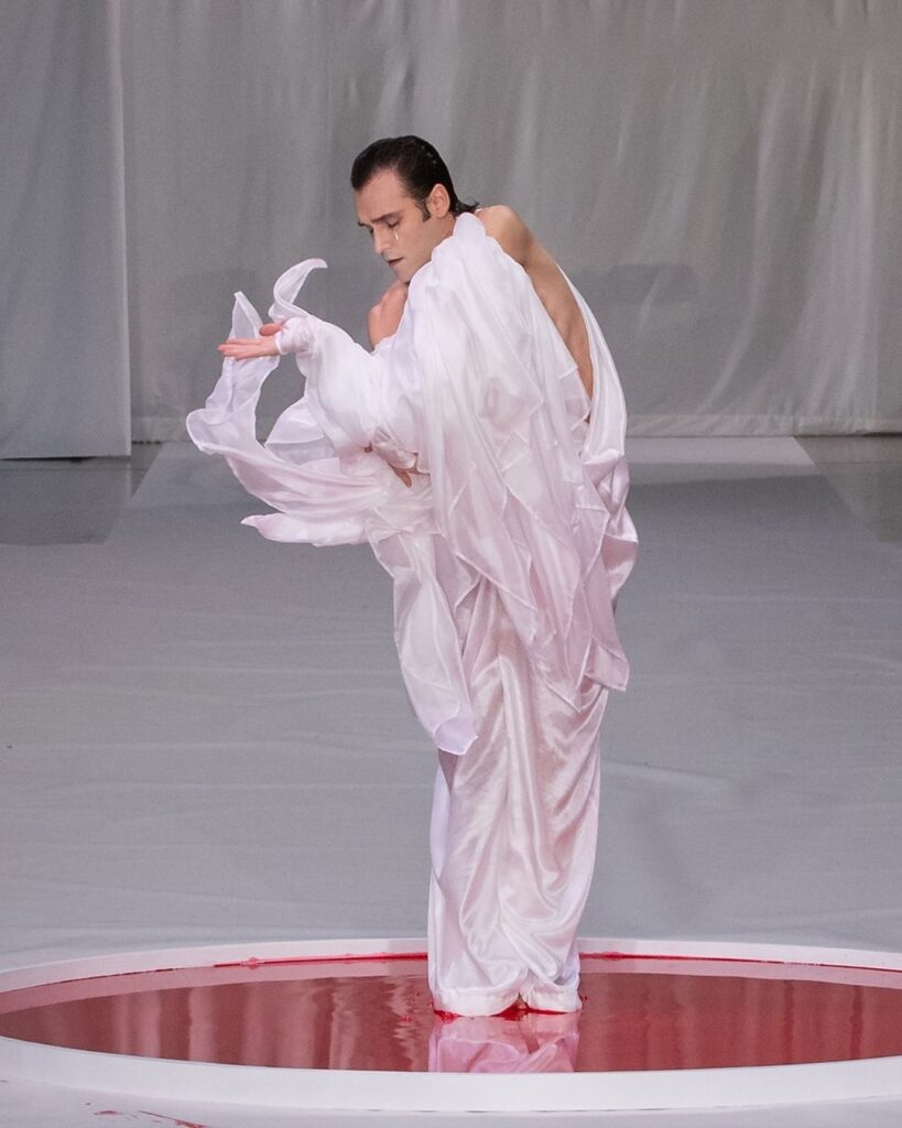 Performance do dançarino Sidi Larbi Cherkaoui em uma piscina vermelha na colução couture "UTAKATA" de Yuima Nakazato