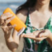 Mulher na praia aplicando protetor solar sob a pele.