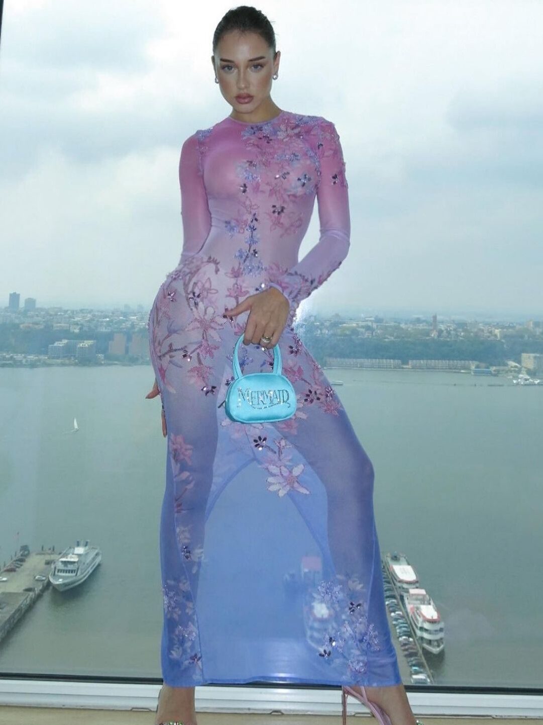 Malu Borges usando um vestido transparente nas cores pastéis em degradê do rosa/roxo para o azul, com bordados de flores. Ainda, acompanha o look uma bolsa em cetim azul escrito "mermaid" em lantejoulas.