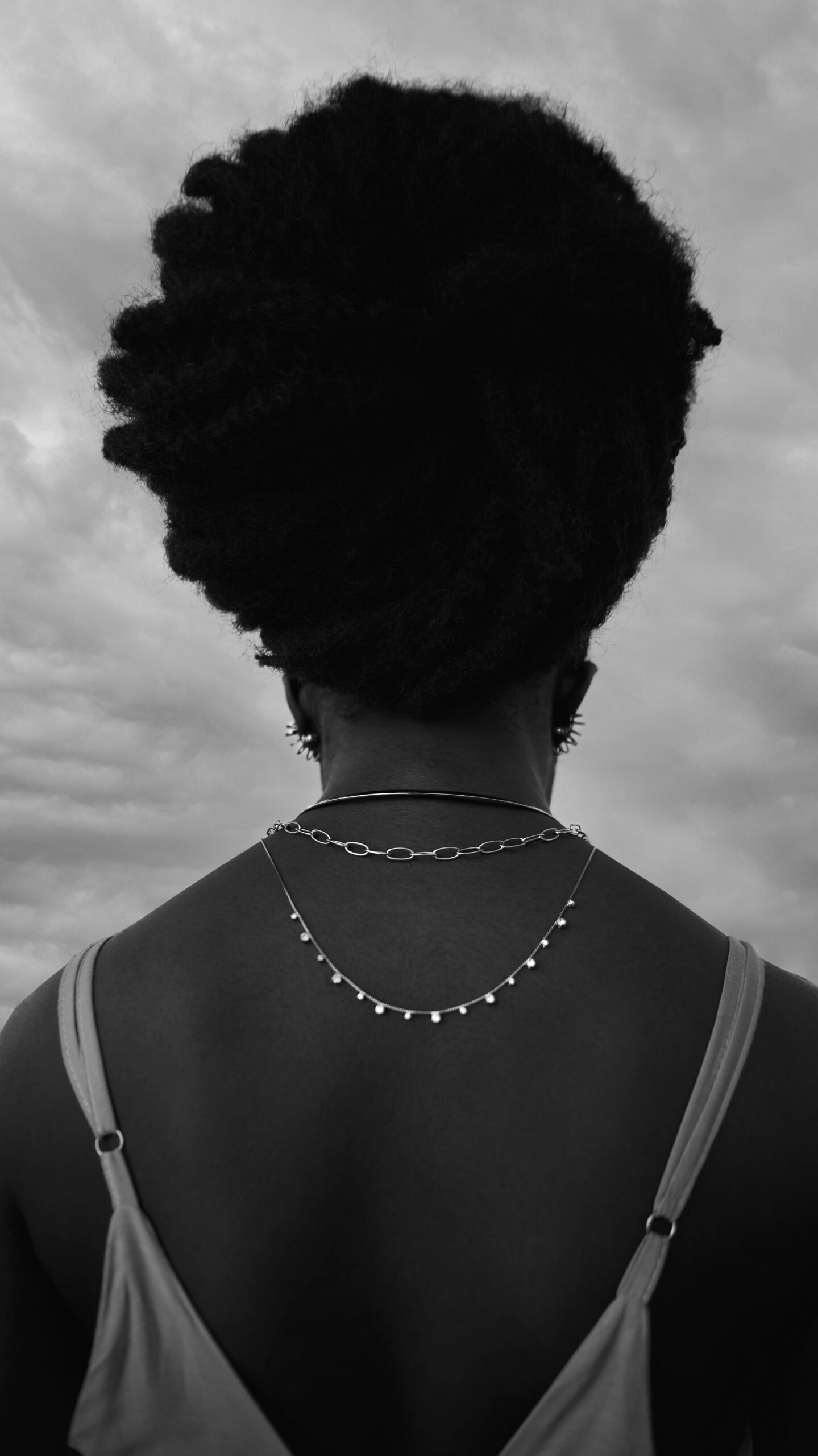 Modelo negra de costas fotograda pelo profissional, os colares se destacam na fotografia preto e branco.
