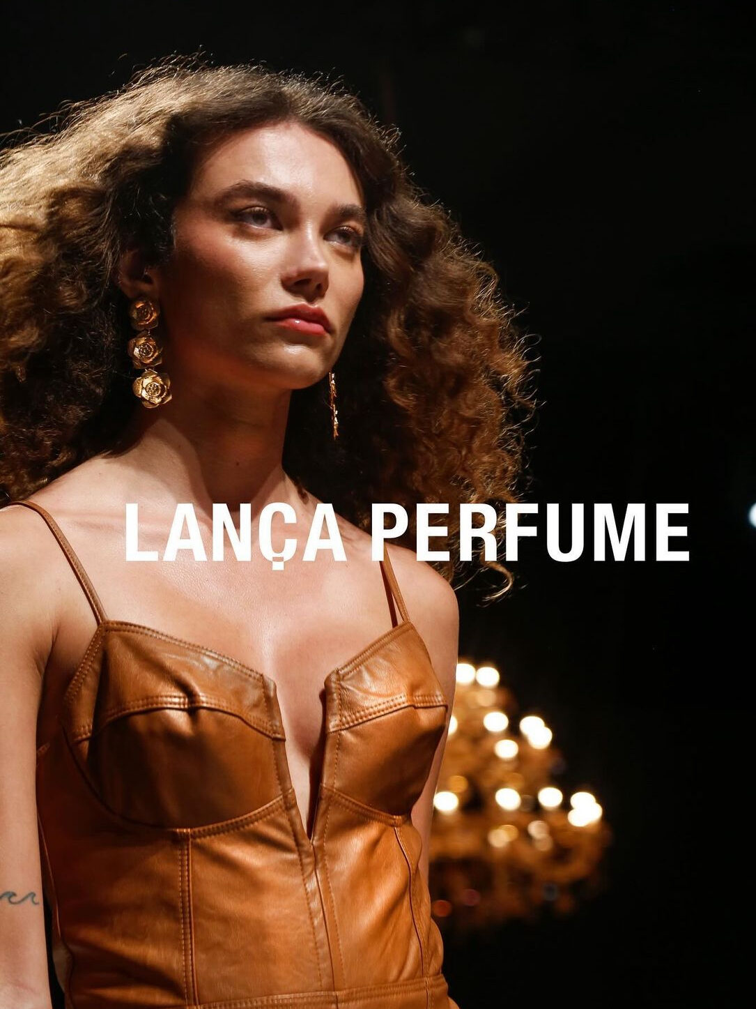 Modelo em fotografia de moda em passarela com uma roupa em couro marrom, por cima da imagem destaca-se "Lança Perfume"