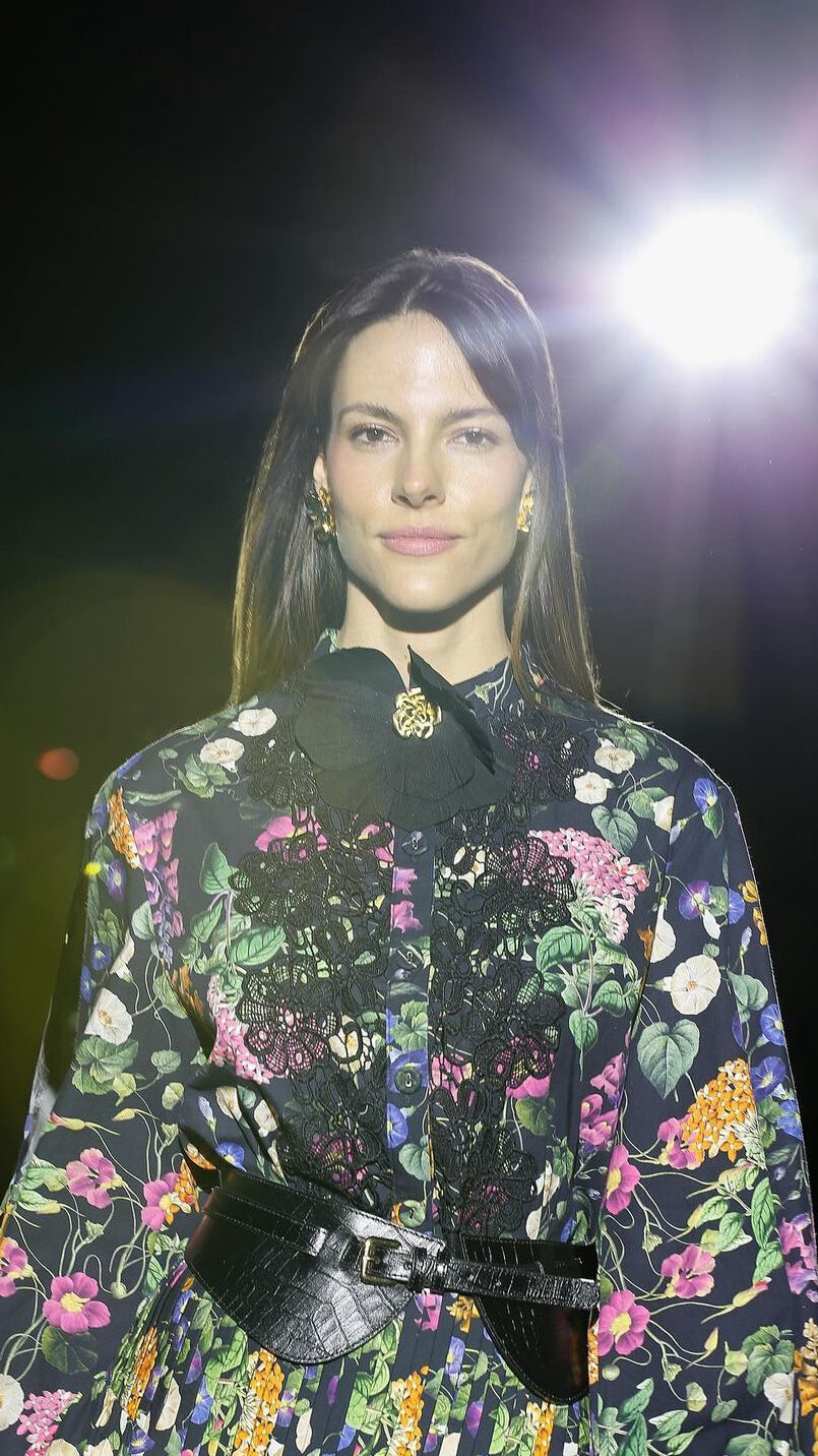 Fotografia de moda de modelo em passarela usando uma blusa florida com renda preta e colar de flor com detalhes dourados.
