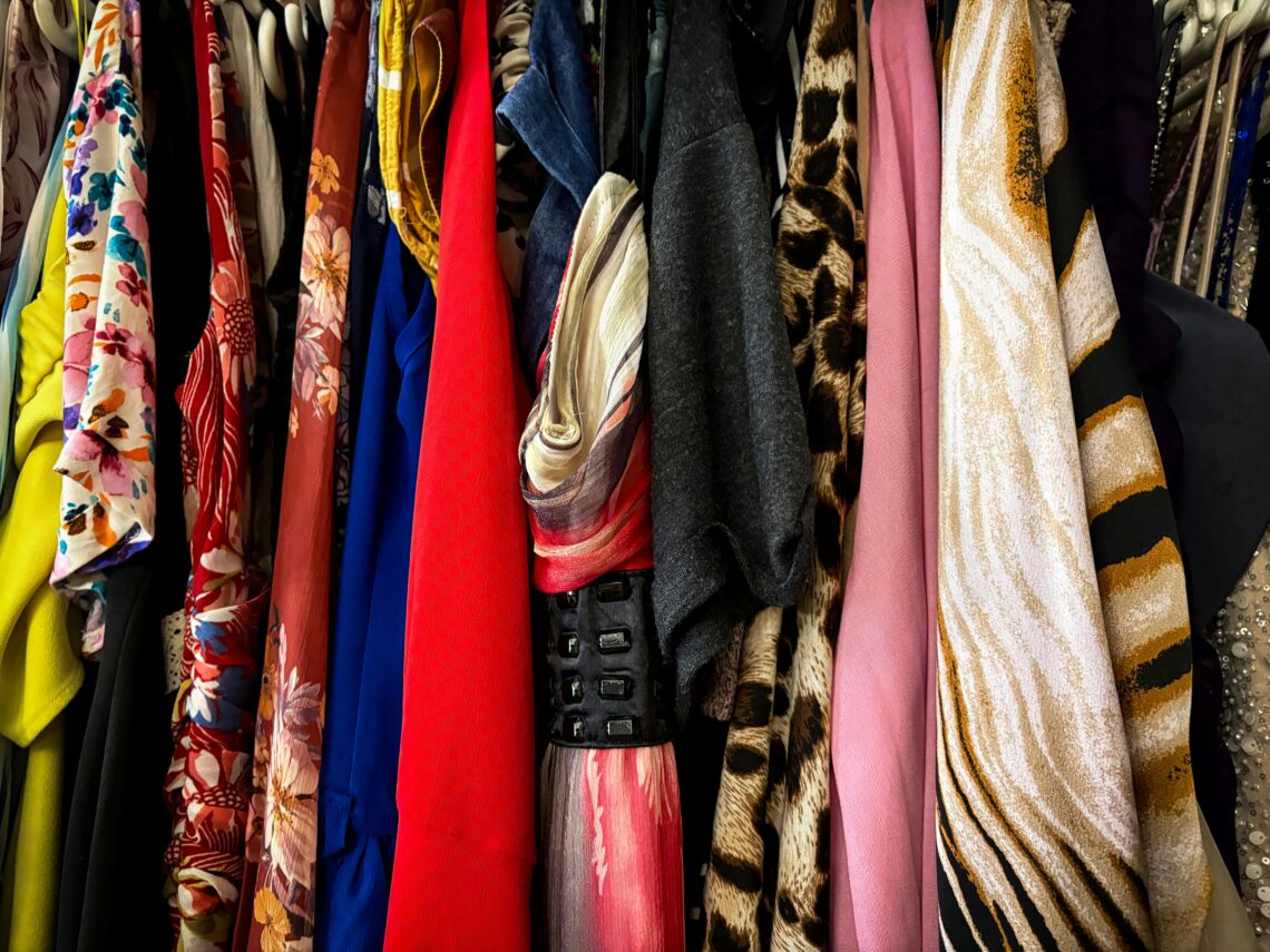 Roupas coloridas e estampadas penduradas em cabides, em um varal, exibindo diversidade de tecidos e estilos.