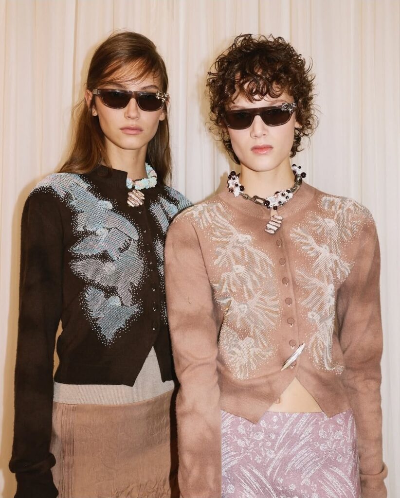 Modelos do desfile Tory Burch na NYFW, usando suéteres, colares e óculos escuros.