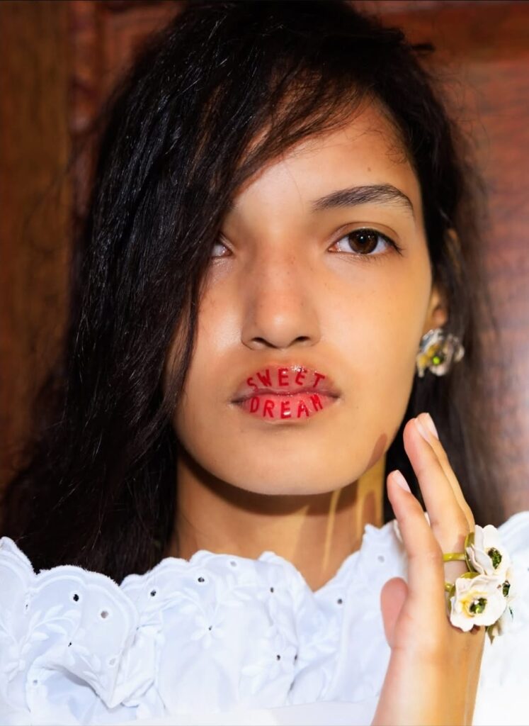 Imagem do desfile Simone Rocha, demonstrando o penteado escolhido e a maquiagem com o dizer Doce Sonho.