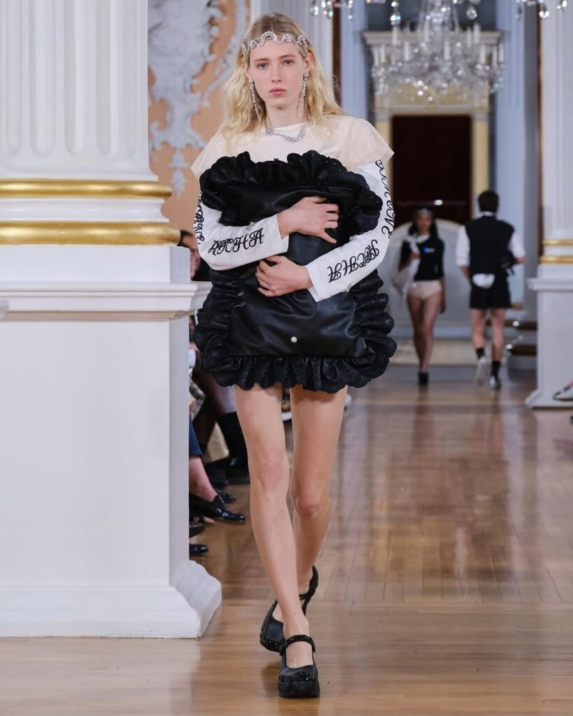 Imagem do desfile Simone Rocha, demonstrando o uso de travesseiros como acessório, complementando a narrativa de sonho.