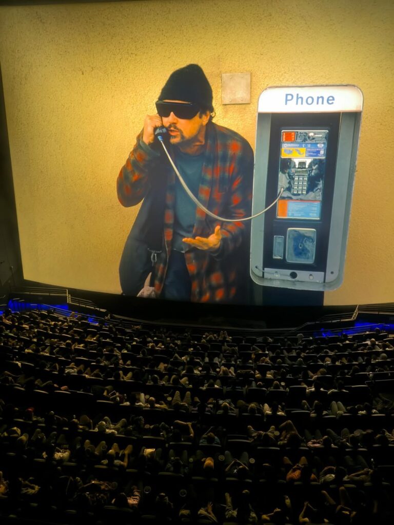 sala de cinema com homem de óculos escuro e blusa listrada;